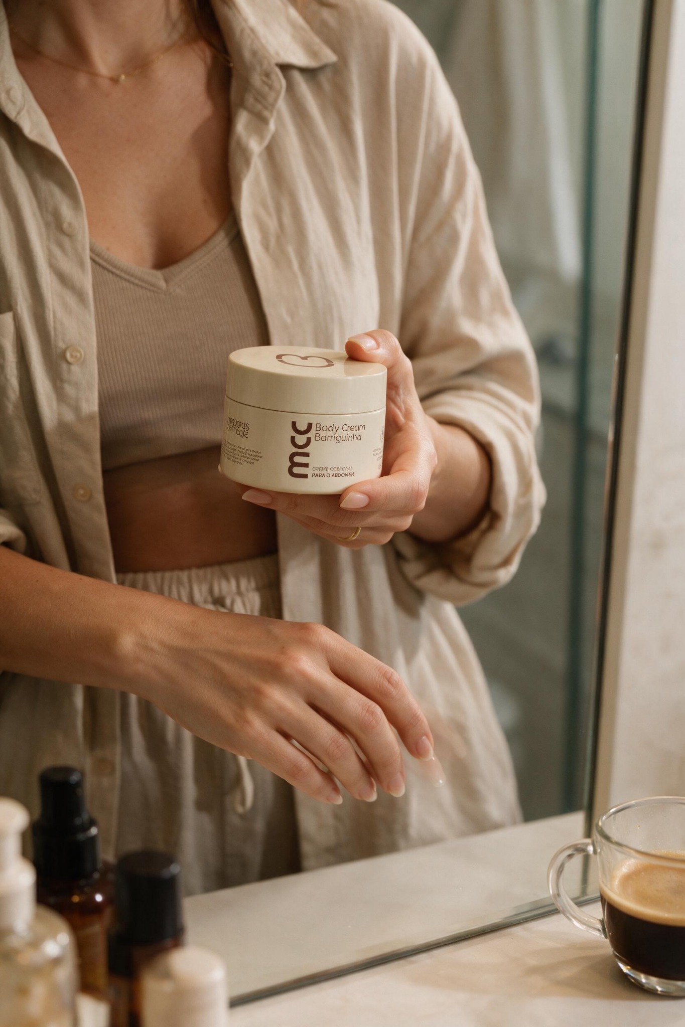 Mulher segurando o Body Cream diante do espelho com café ao lado